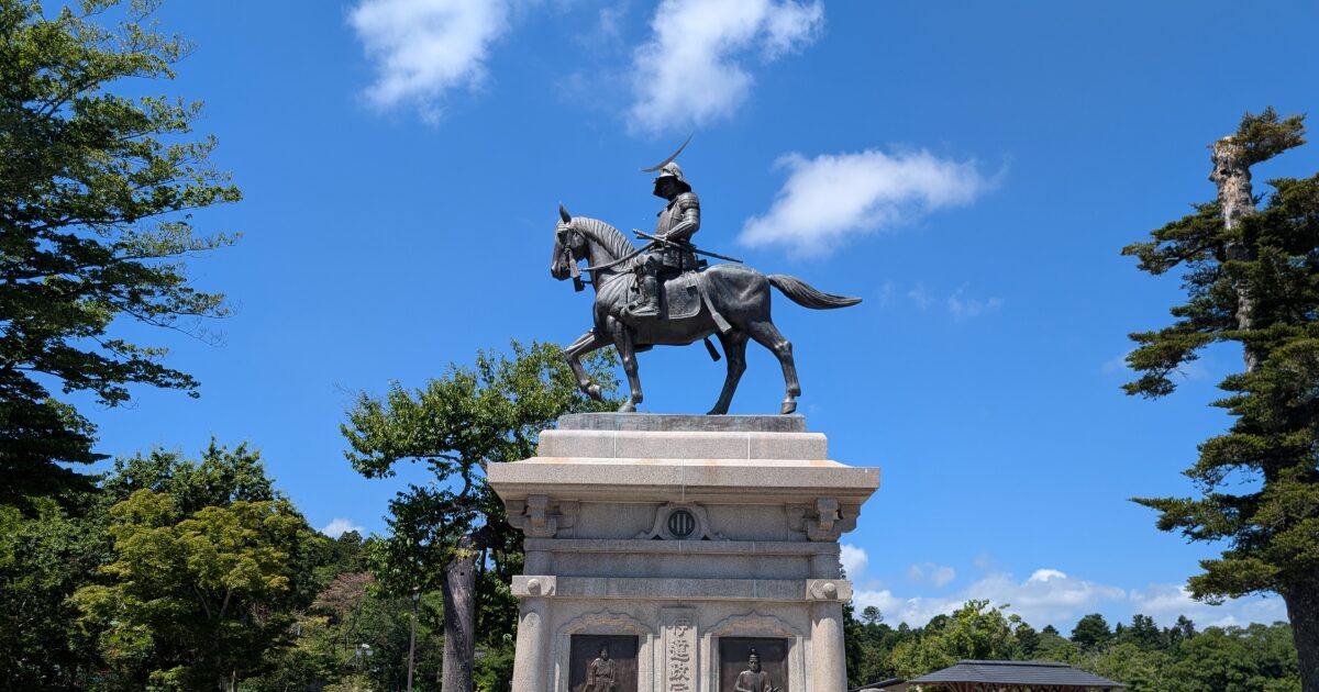 青空の下に建つ伊達政宗騎馬像と周囲の緑